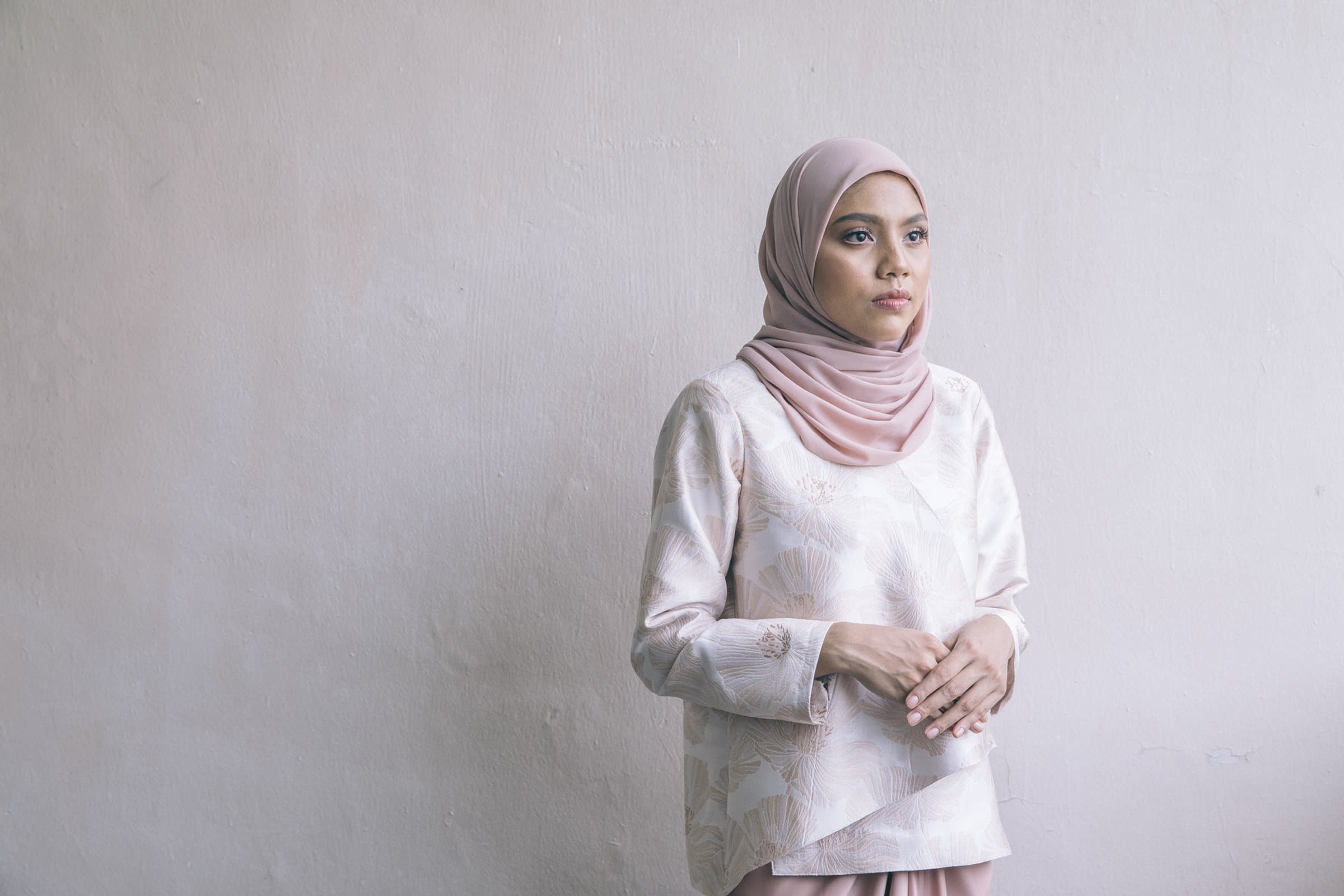 A model in a blush floral kurung top against a pale wall