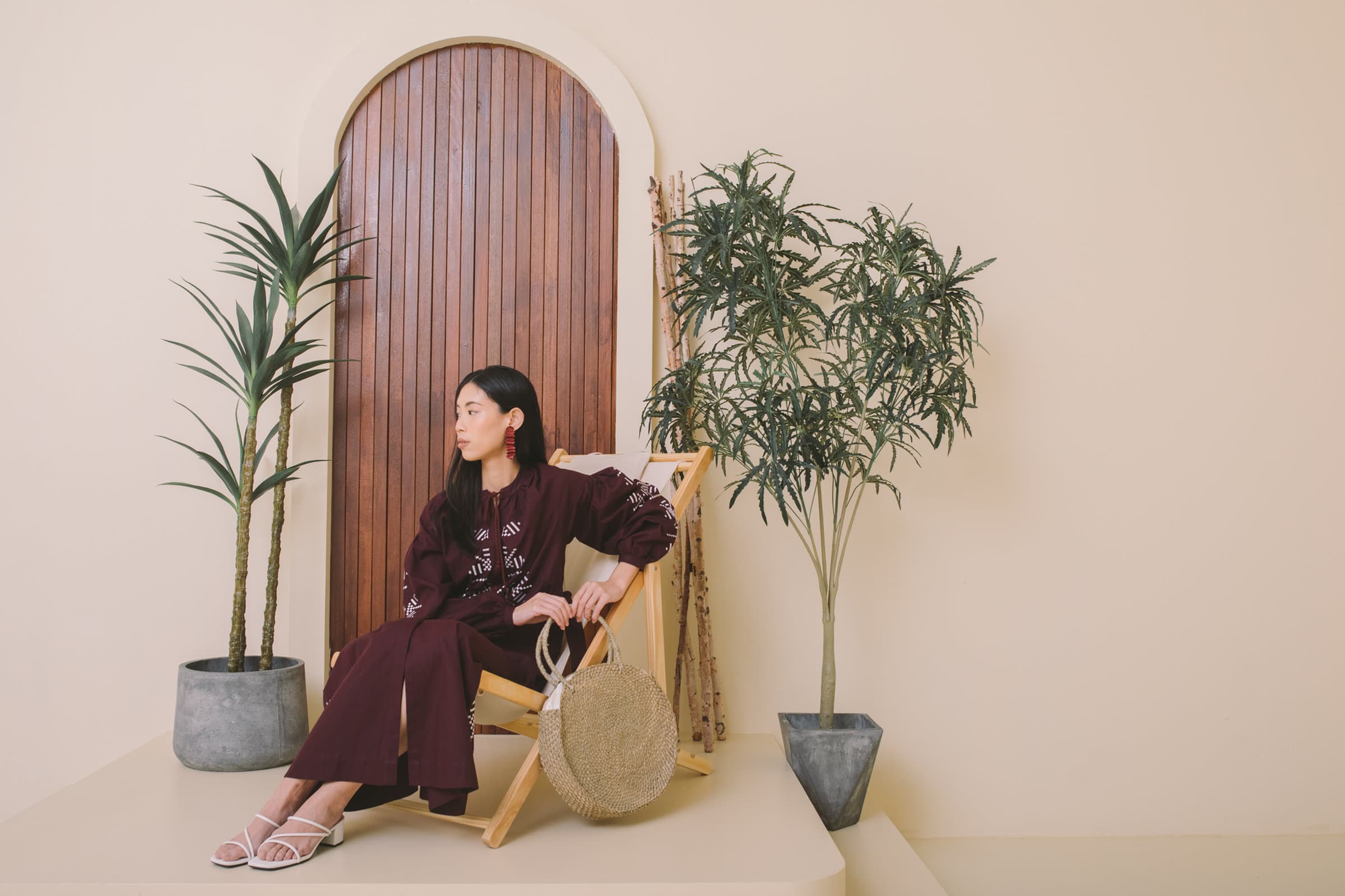 A model in a plum embroidered dress seated before an arched wooden door