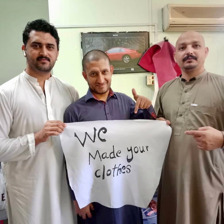 Three of our makers holding a sign that reads “We made your clothes”